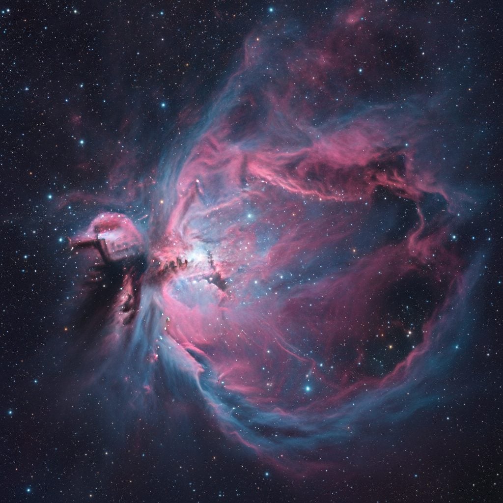Orion Nebula (M42) showing colorful pink and blue gas clouds of an active stellar nursery against a deep navy starry background.