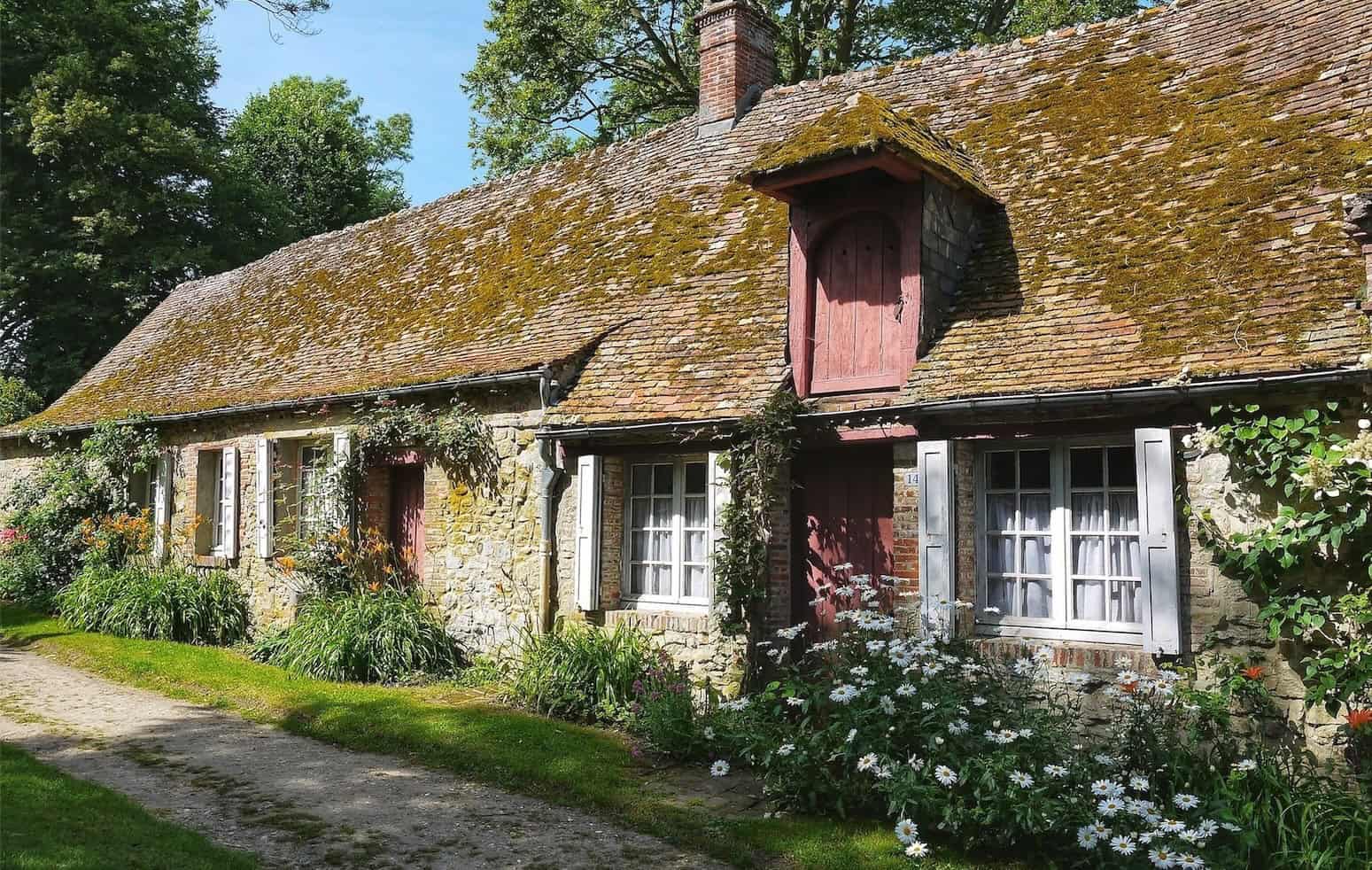 Historic stone house with small windows and moss-covered roof in a rural setting.