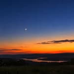 Venus visible after sunset over a scenic landscape with trees and water.