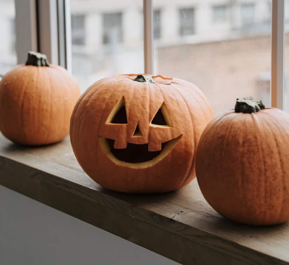 Three pumpkins, one carved with a smiling face, on a windowsill for Halloween decor.