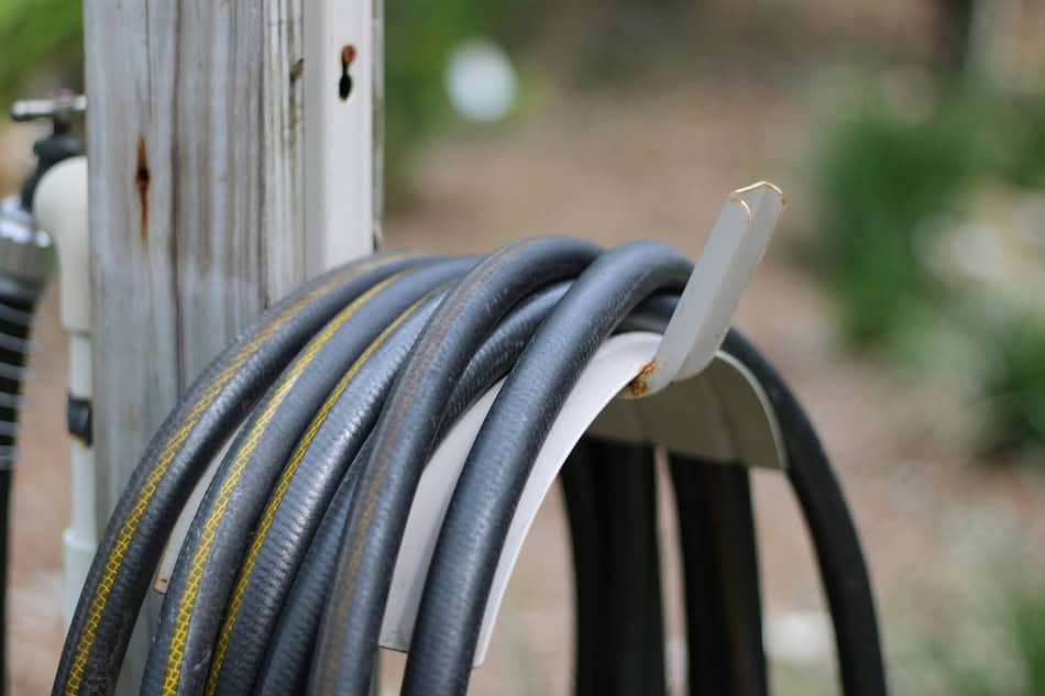 Garden hose coiled on a wall hook in a garden setting.