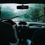 View of two drivers inside a car with foggy windshield during rain.