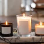Three lit candle jars on a marble tray in cozy home setting.