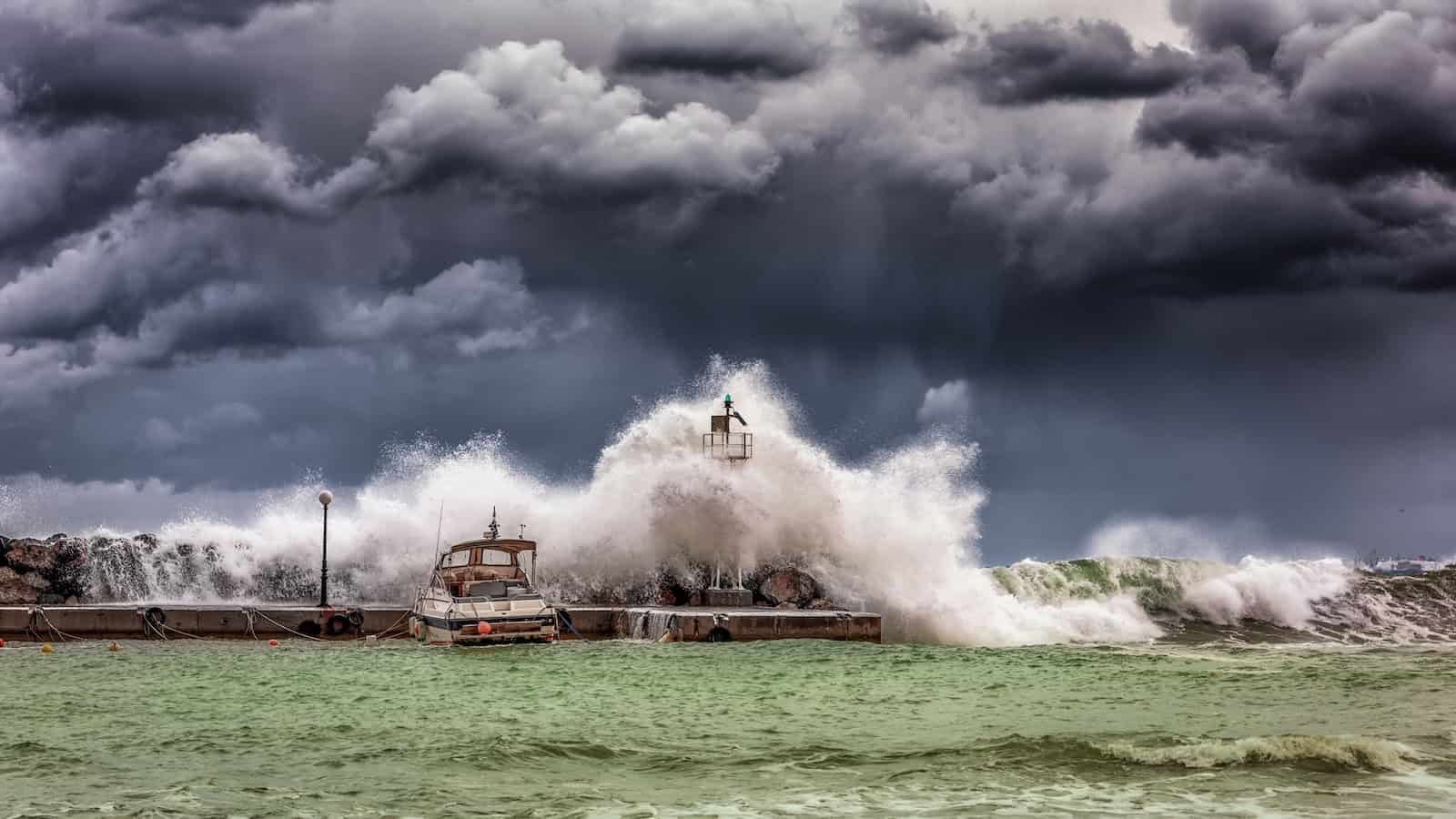 Stormy ocean scene with large waves crashing against a pier and dark storm clouds overhead.
