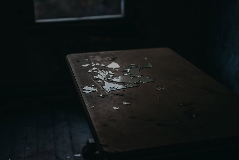 Broken mirror shards on a dark wooden table in a dimly lit room.