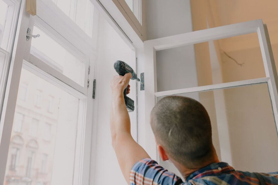 Man fixing window screen with a screwdriver in a bright room.