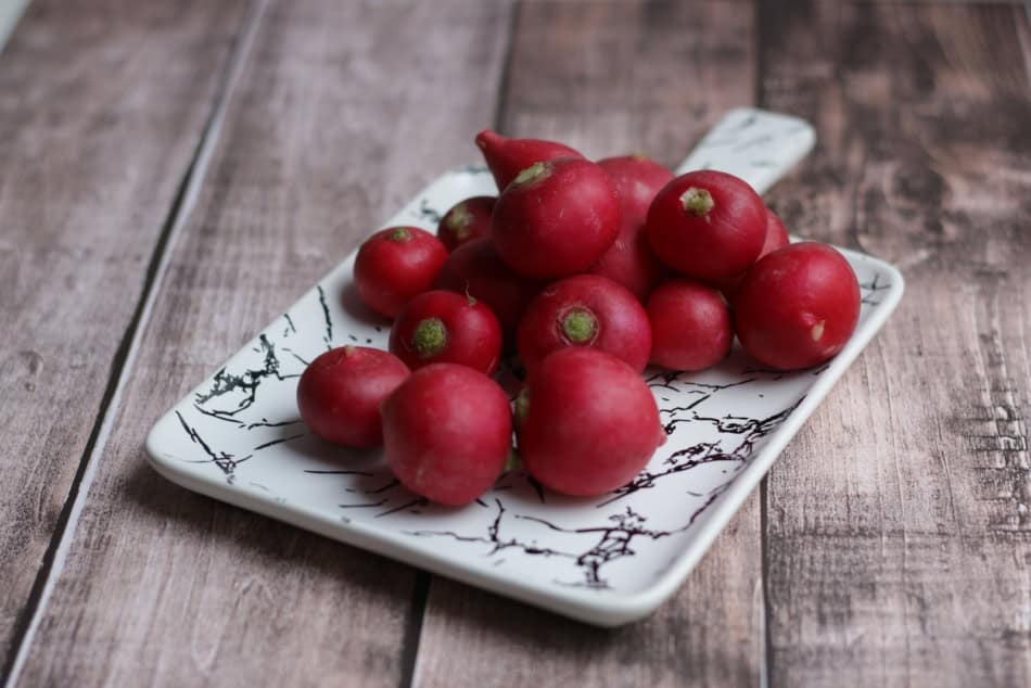 Fresh red radishes on a decorative plate for gardening and cooking.