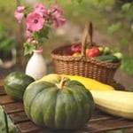 Fresh pumpkins and squash on a rustic wooden table in an outdoor garden setting.