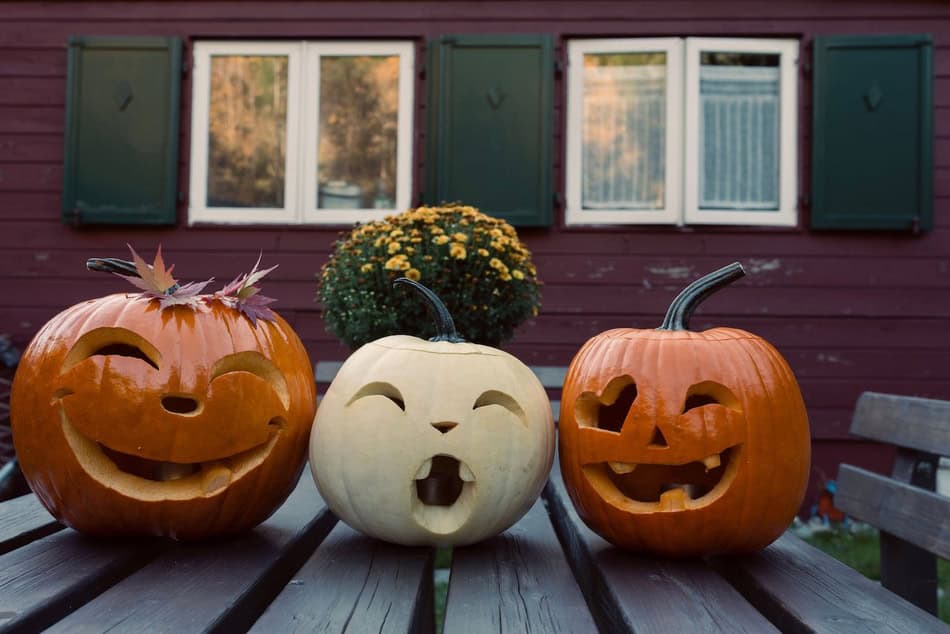 Three carved pumpkins with different faces on a wooden table outside.