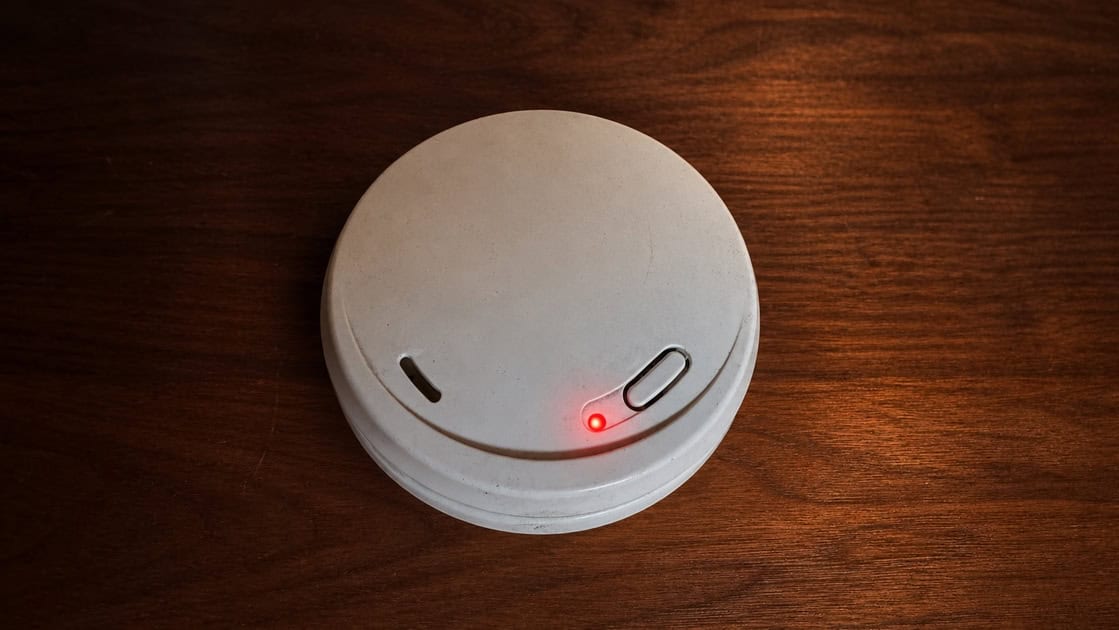 Wireless smoke alarm with red LED indicator on wooden surface.