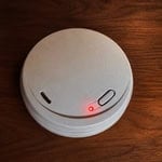 Wireless smoke alarm with red LED indicator on wooden surface.