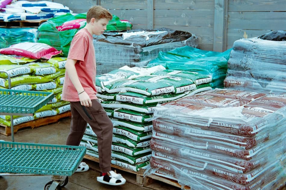 Young boy shopping for garden soil and fertilizer at outdoor store.