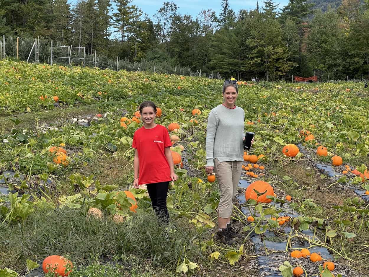 Two women and a girl in a pumpkin patch with ripe pumpkins ready for harvest.