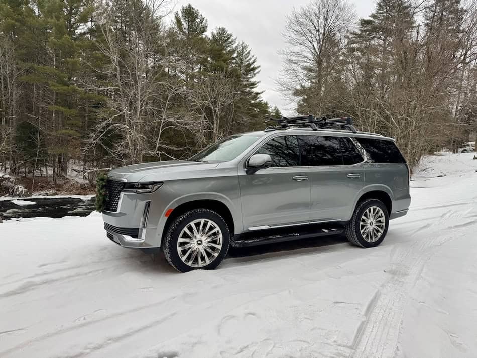 Silver SUV parked on snowy road with snow tires in winter forest.