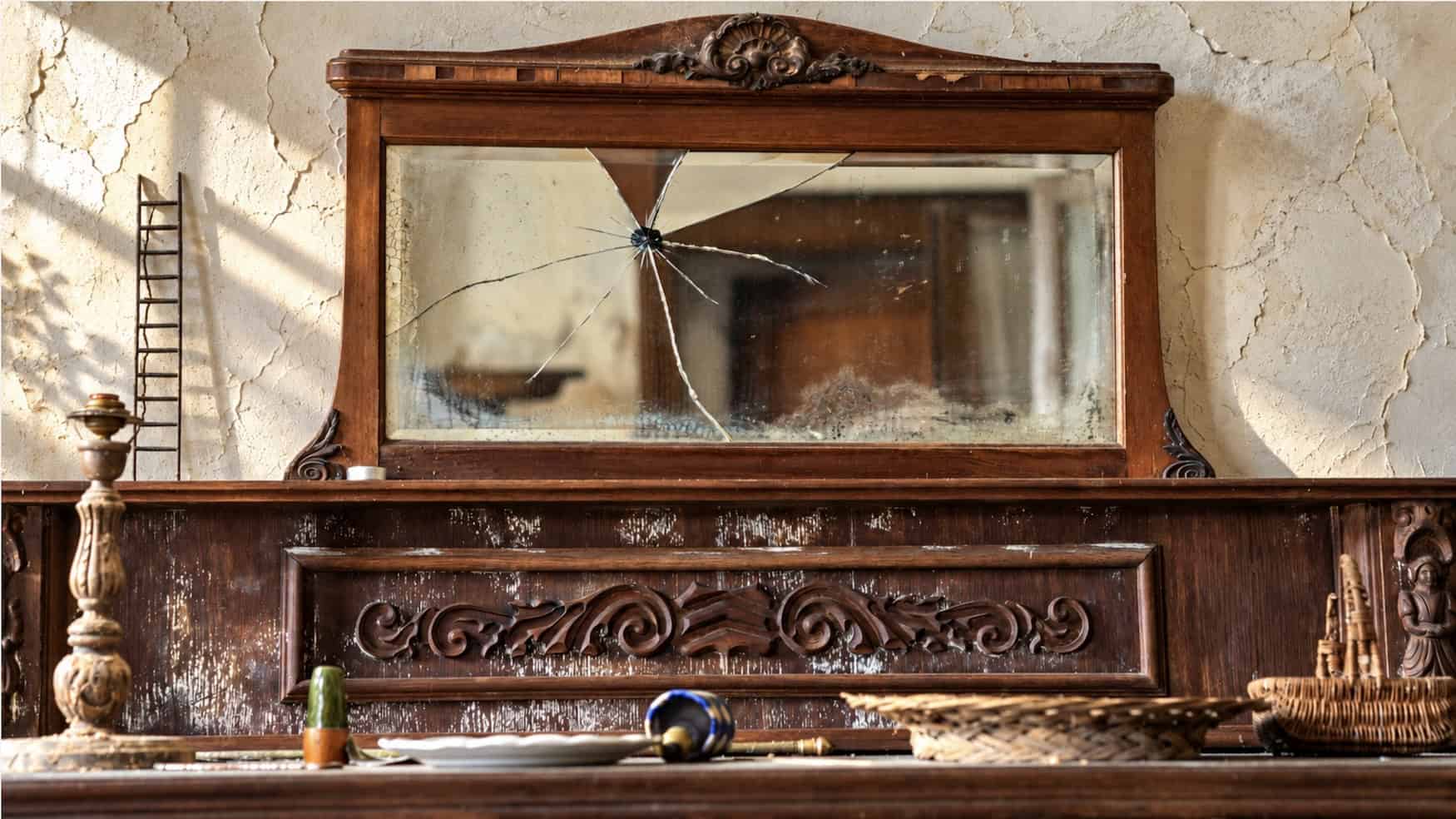 Vintage wooden mirror with cracked glass and ornate carvings.