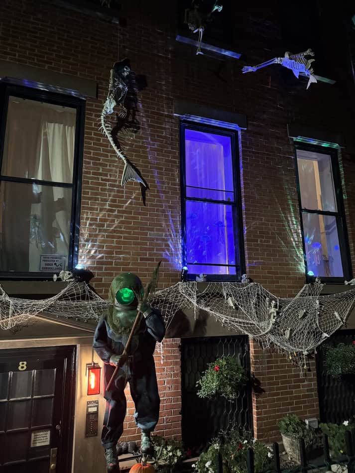 Spooky Halloween scene with hanging skeletons and spider webs on brick building.