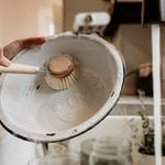 Person washing a dish with soap and a scrub brush in the kitchen sink.