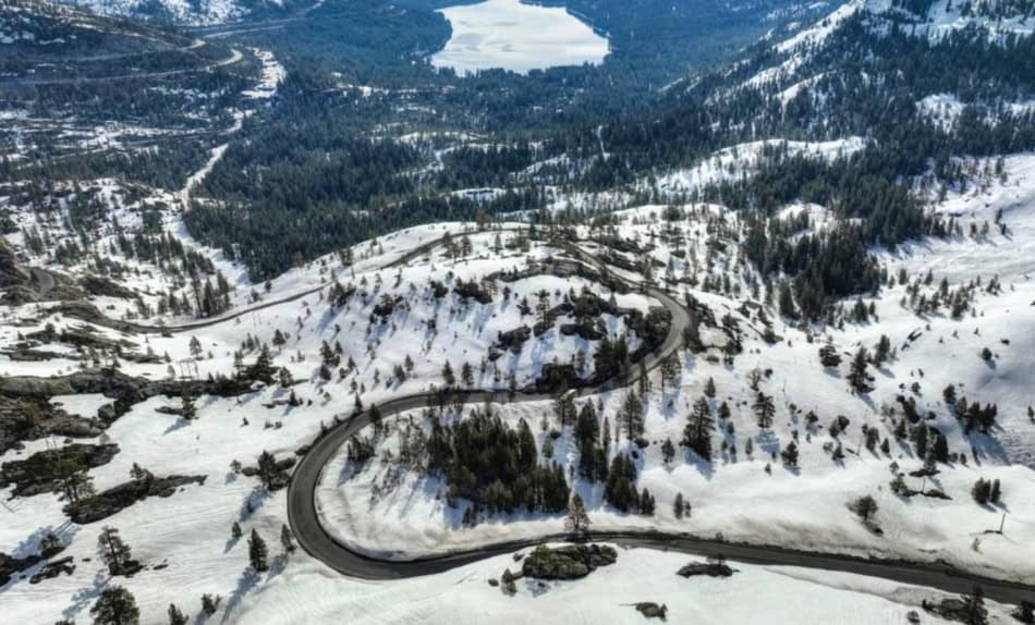 Winding mountain road through snow-covered hills and trees.