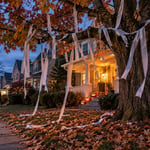 Front porch with Halloween decorations and streamers on a tree in autumn evening.
