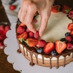 Hand placing fresh berries on a chocolate cake with strawberries and blueberries.