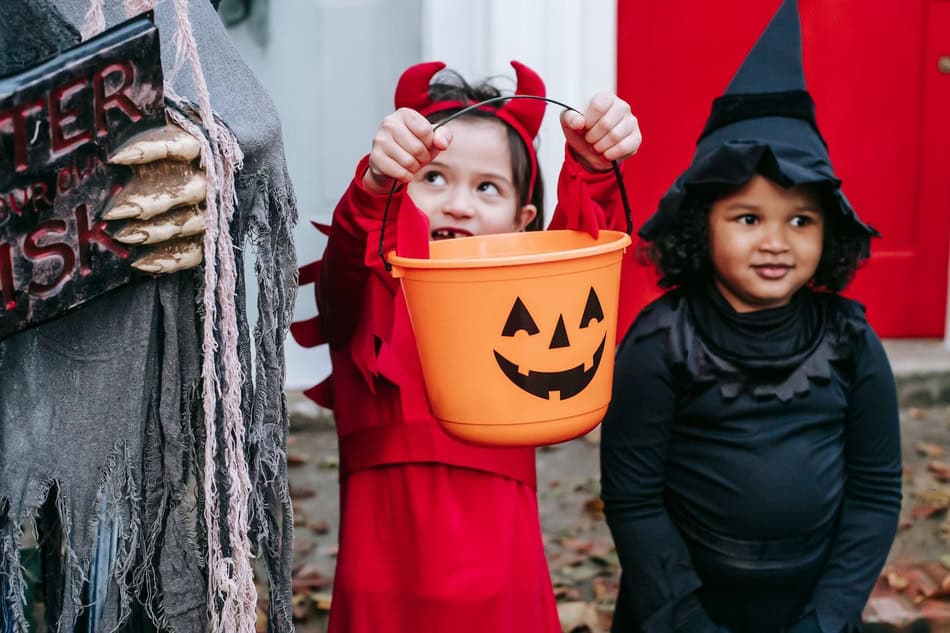 Children in Halloween costumes with pumpkin bucket and witch hat.