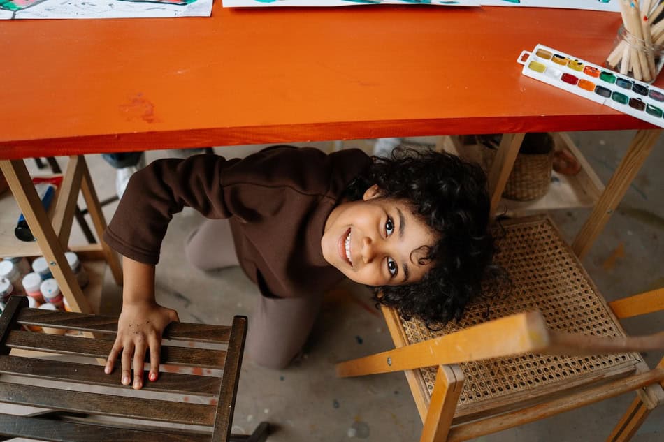 Young child smiling while painting at an art table with chairs.
