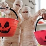 Children dressed as mummies holding Halloween pumpkin buckets.