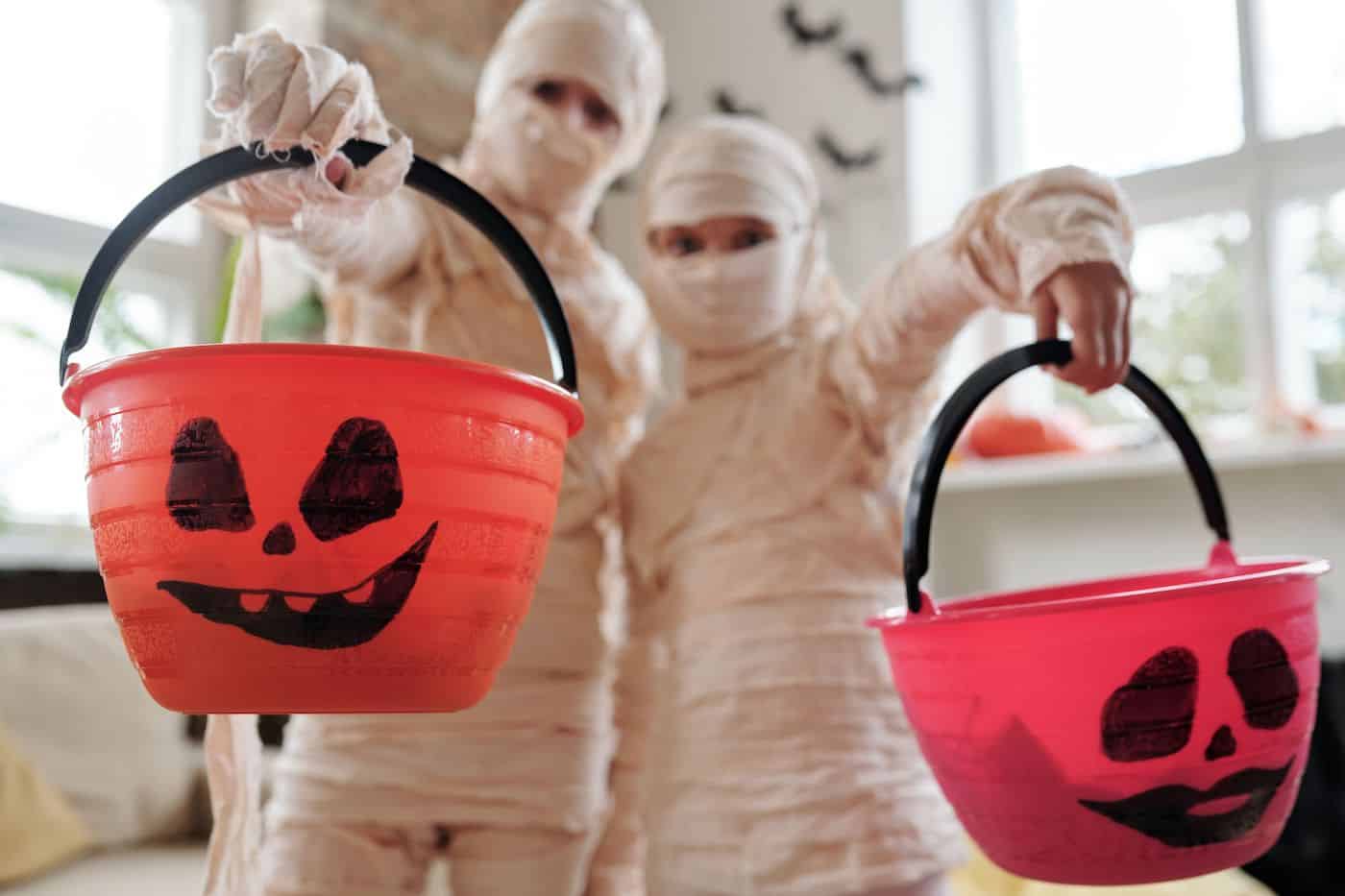 Children dressed as mummies holding Halloween pumpkin buckets.