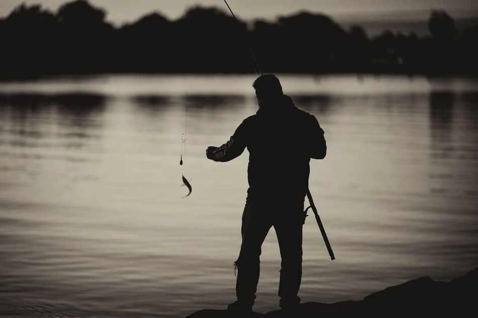 Silhouette of a fisherman fishing at sunset on a calm lake.