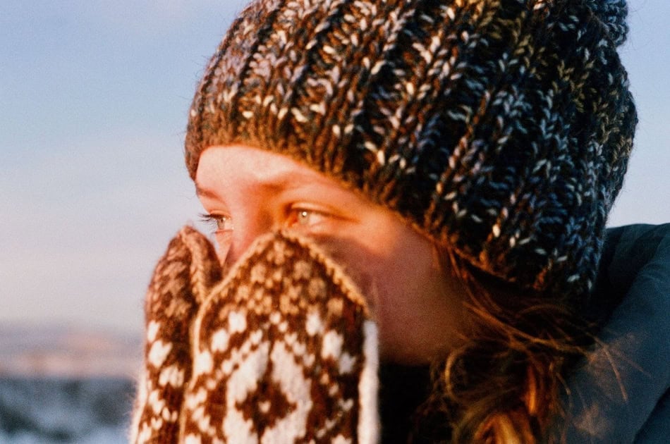 Girl in winter hat and mittens shielding her face from cold air.