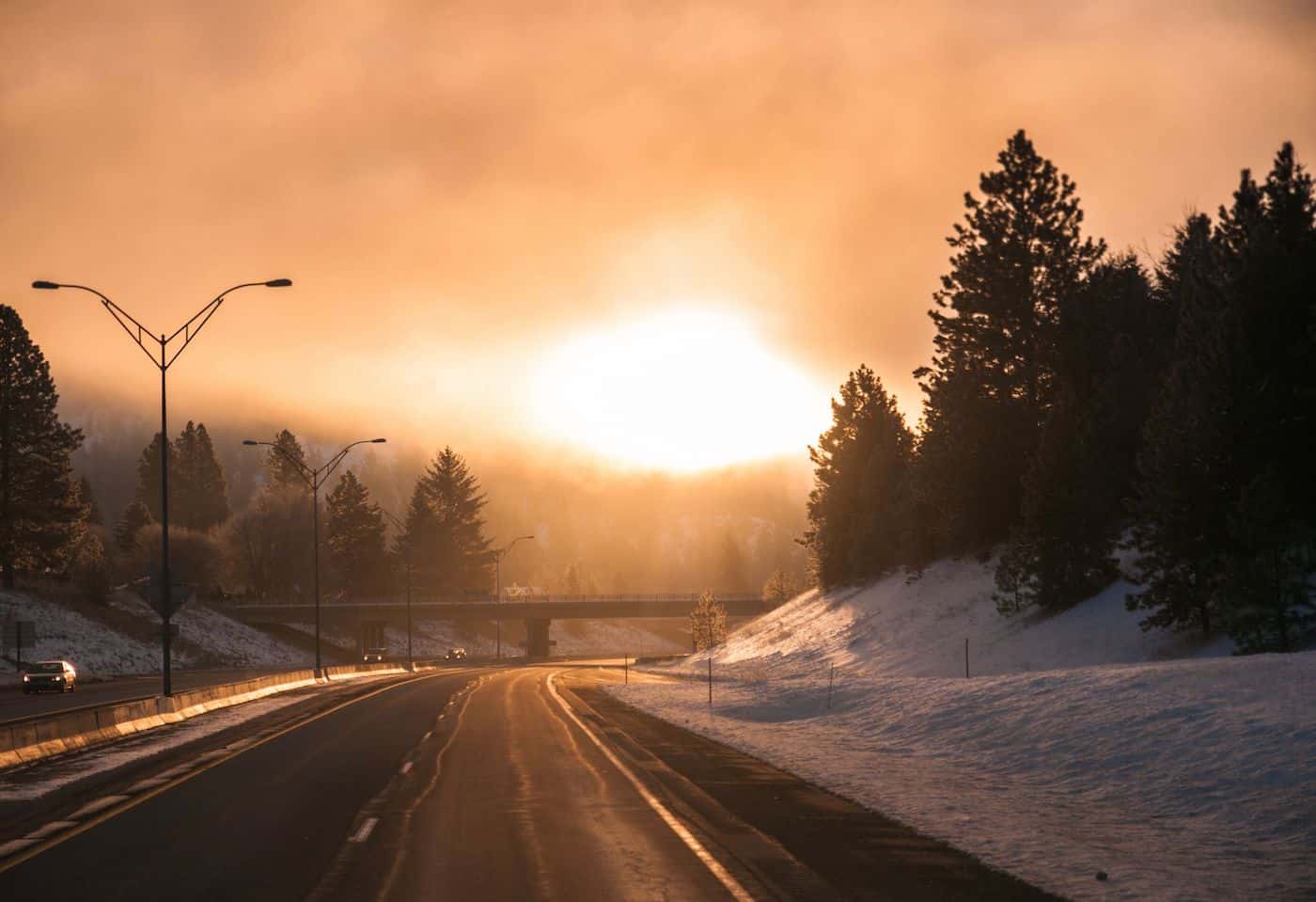 Bright sun setting over a snowy landscape with trees and a highway.