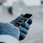 Person holding smartphone with gloves in cold weather.