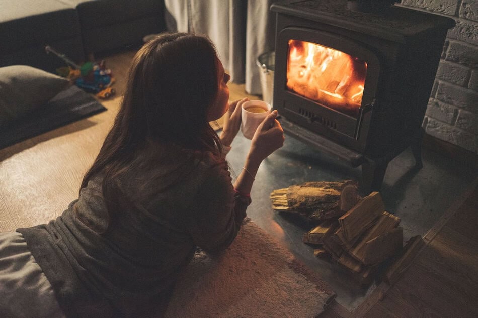 Woman enjoying a warm drink by a lit fireplace in a cozy living room.