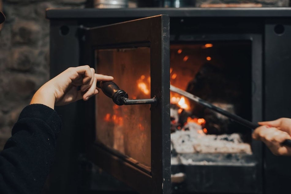 Person collecting firewood near a cozy fireplace in winter.