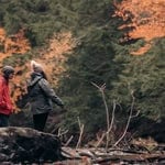 Two people bird watching in a forest during fall with colorful leaves.