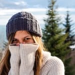 Woman wearing a knit hat and sweater in a snowy outdoor setting.