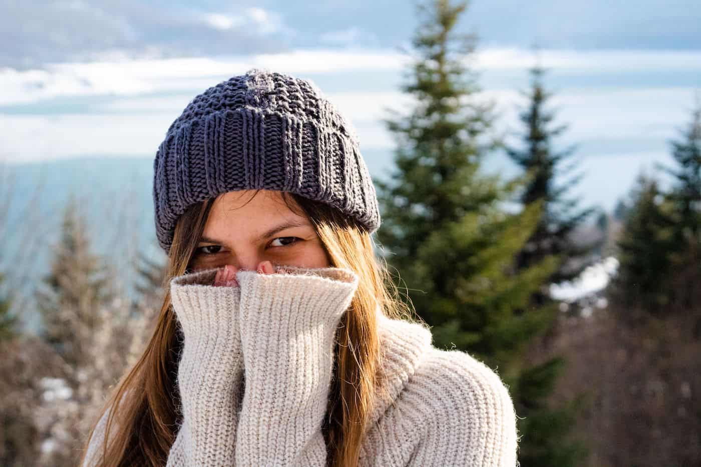 Woman wearing a knit hat and sweater in a snowy outdoor setting.