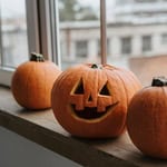 Three pumpkins on a windowsill, one carved with a jack-o'-lantern face.