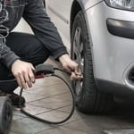 Person inflating car tire with air compressor in garage.