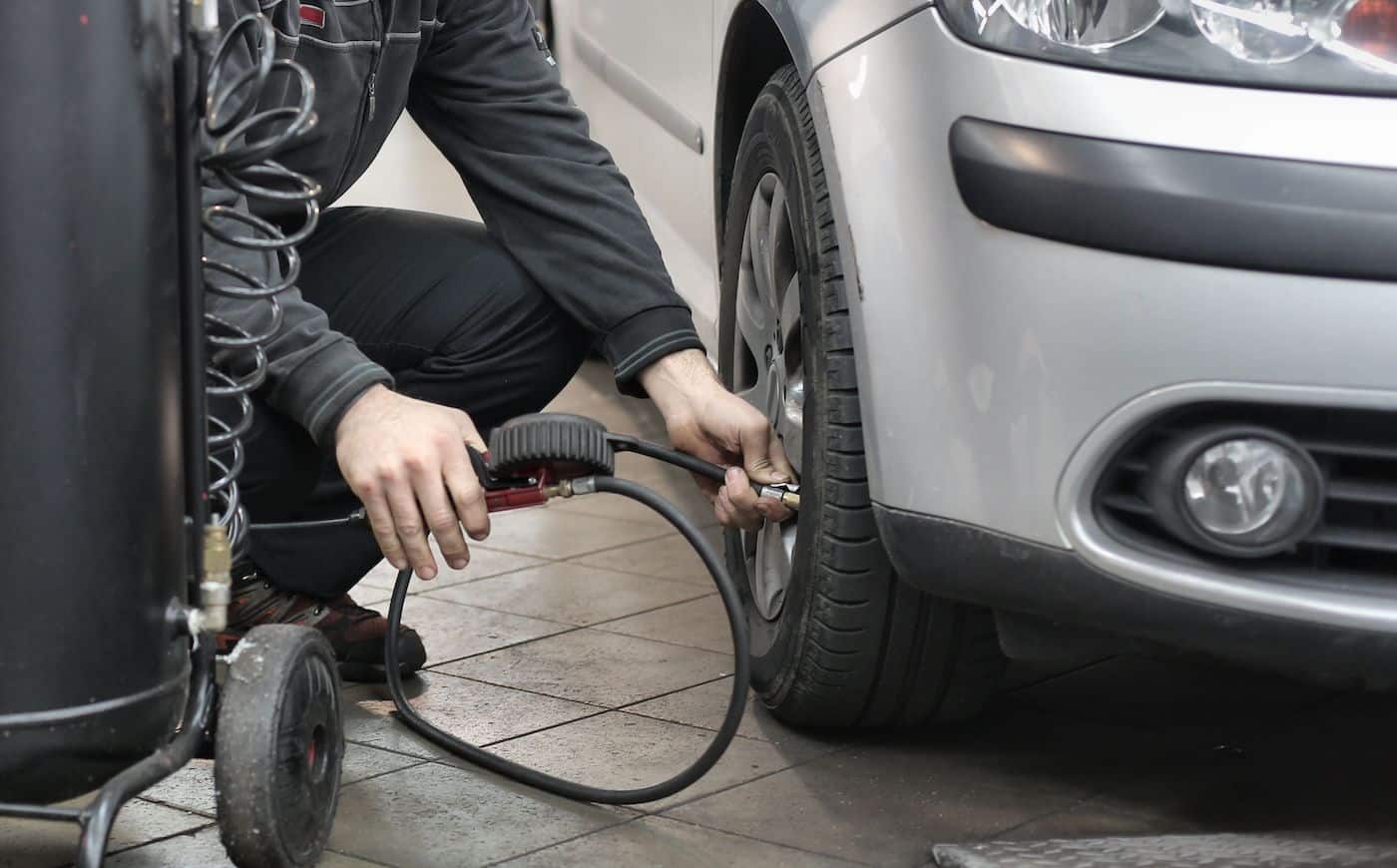 Person inflating car tire with air compressor in garage.