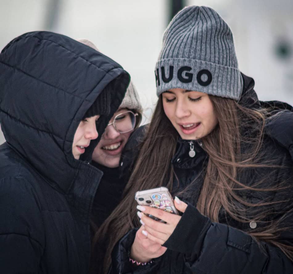 Young friends in winter clothing looking at a smartphone together.
