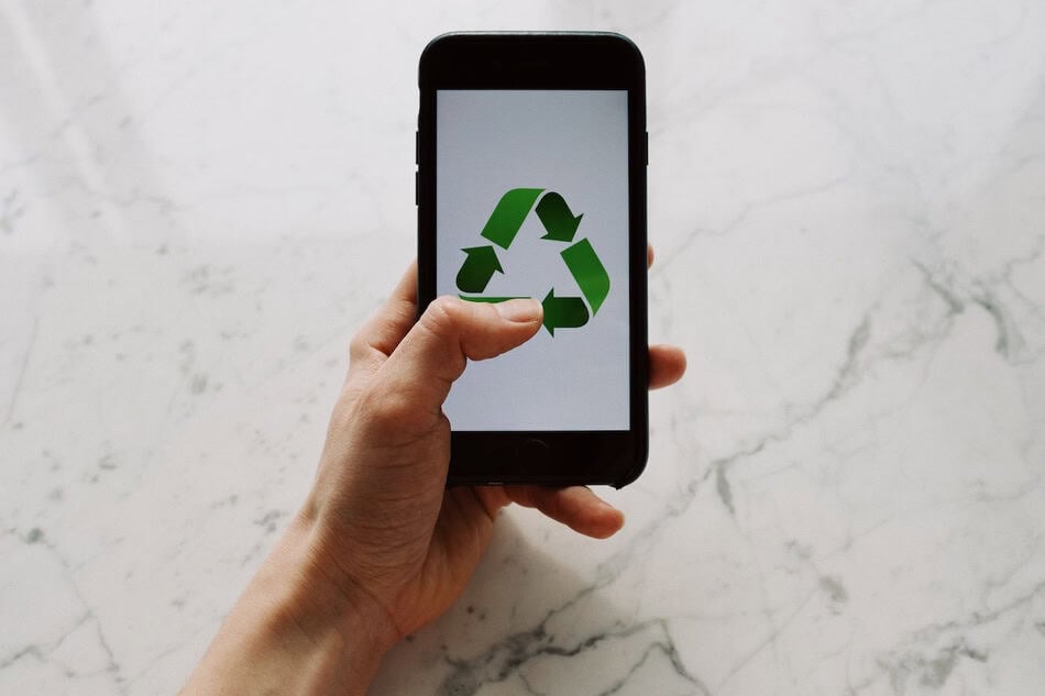 Hand holding smartphone displaying recycling symbol on a marble surface.