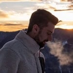 Man exhaling visible breath during cold morning sunset outdoors.