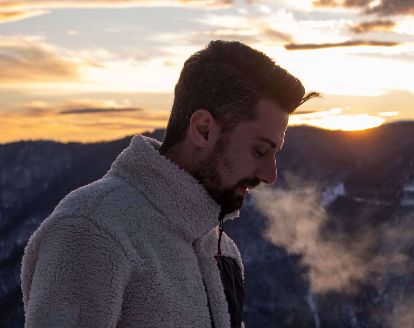 Man exhaling visible breath during cold morning sunset outdoors.
