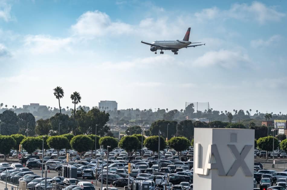 Airplane approaching over a busy LAX parking lot and terminal sign.
