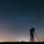 Person using a telescope under a starry night sky.