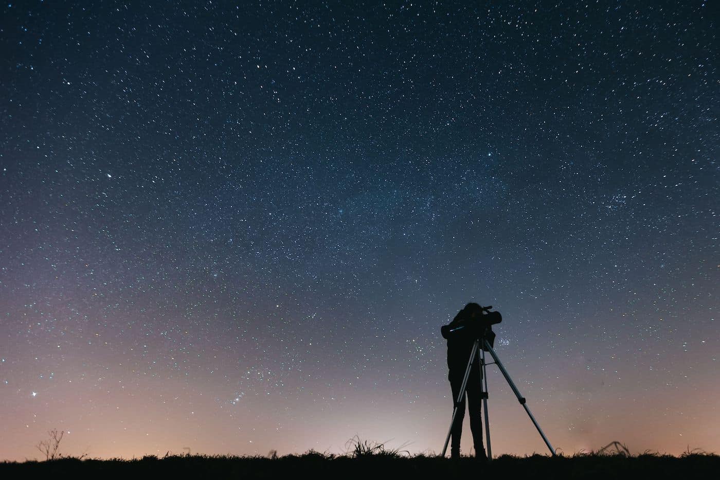Person using a telescope under a starry night sky.