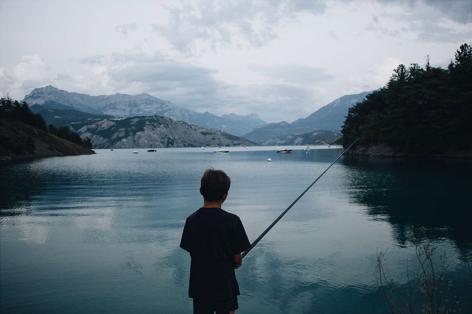 Child fishing in a calm mountain lake with scenic background.